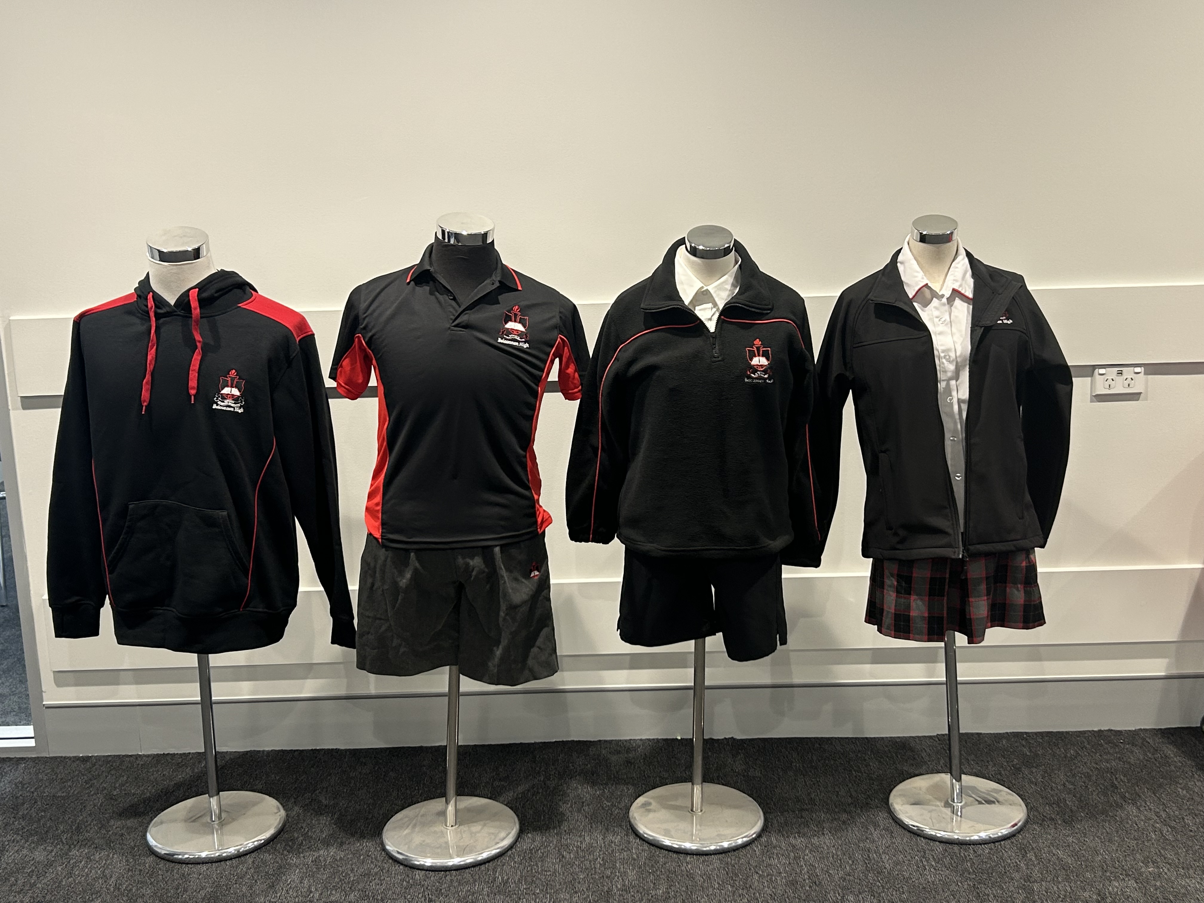 Belconnen High School uniform display: 1. Black hoodie with red shoulder accents. 2. Black and red polo shirt with dark grey shorts. 3. Black half-zip fleece over a white shirt with black shorts. 4. Black zip-up jacket over a white shirt with a red and black pleated plaid skirt.